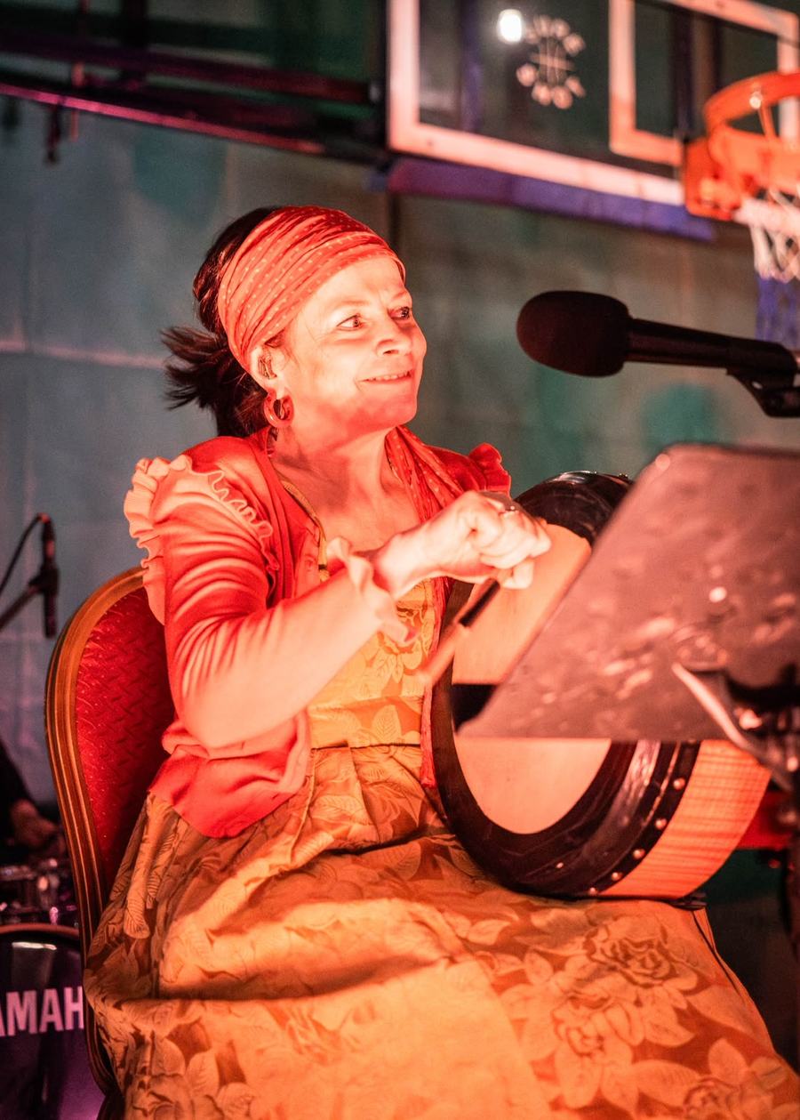 A musician in a headscarf smiling behind a bodhrán.