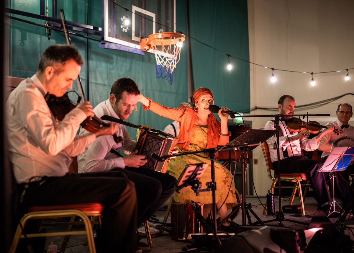 The Gralton Big Band playing in a hall, fiddles, accordion and a singer in orange.