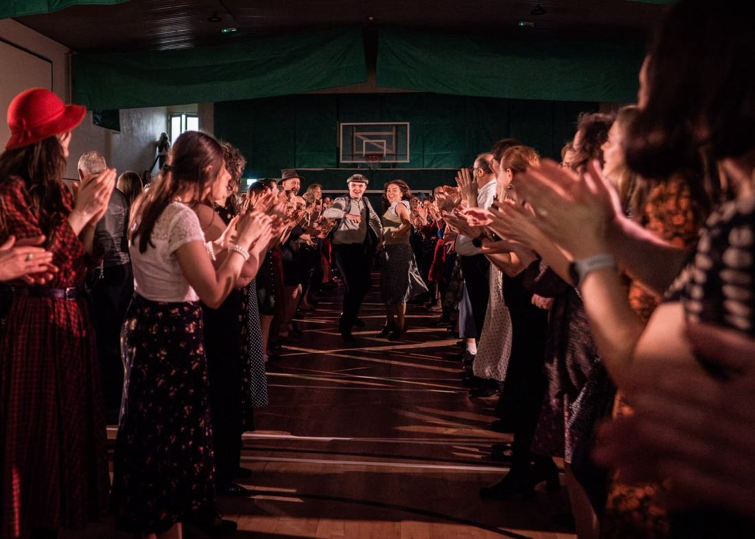 Two lines of dancers clapping as a couple comes down the middle of the floor.