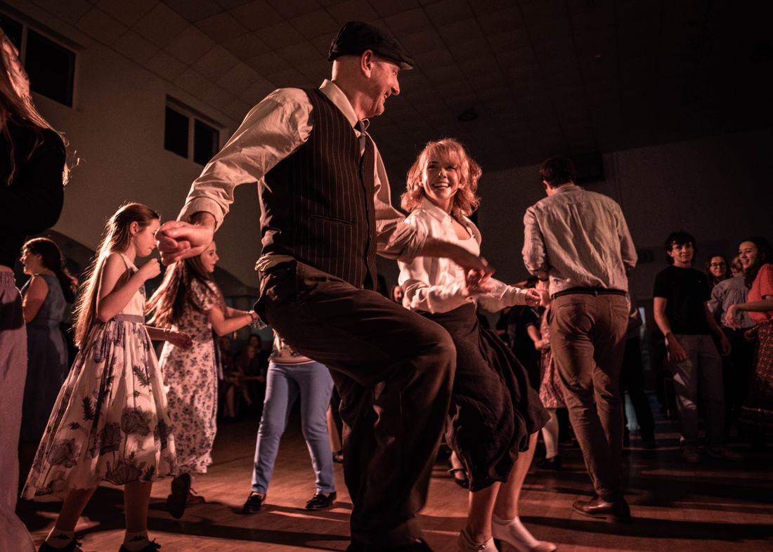 A man in a waistcoat swinging his partner clean off the ground.
