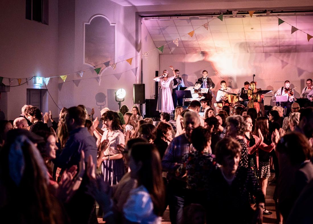 A full hall dancing under coloured lights with bunting overhead.